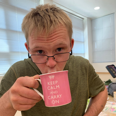 man in green shirt drinks from a pink mug with words "keep calm and carry on"