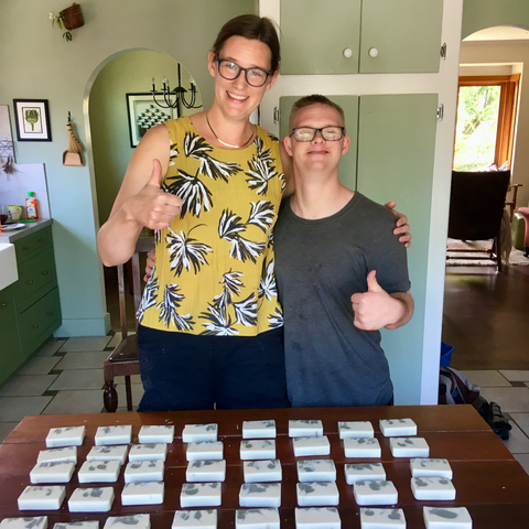woman and man stand behind table full of bars of soap giving a thumbs up