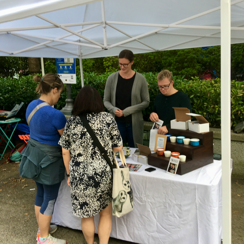 Two people talking to Caroline and Simon at a market table under a white tent