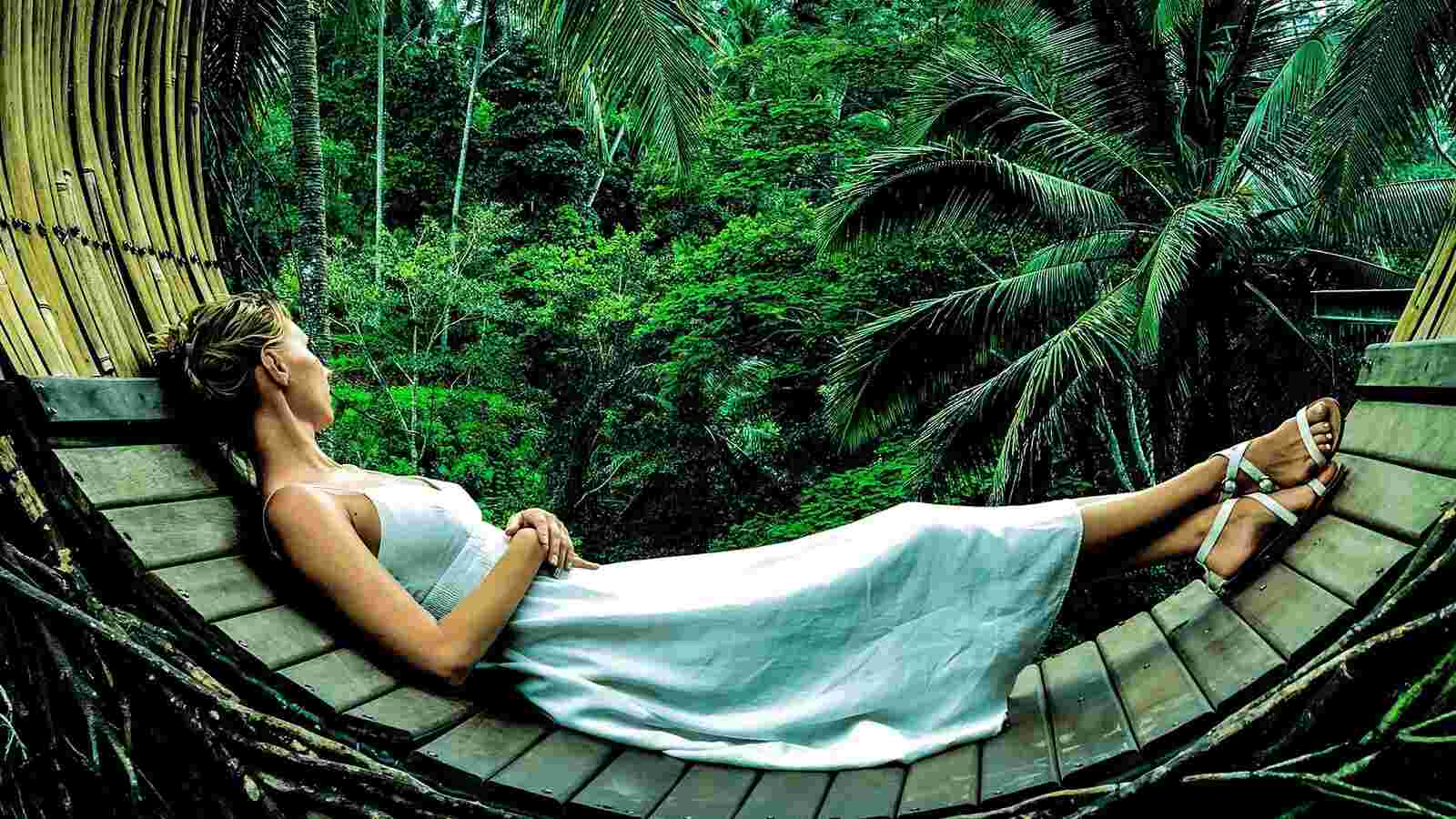 a young woman in white dress resting in a hammock with vivid green forest in the background