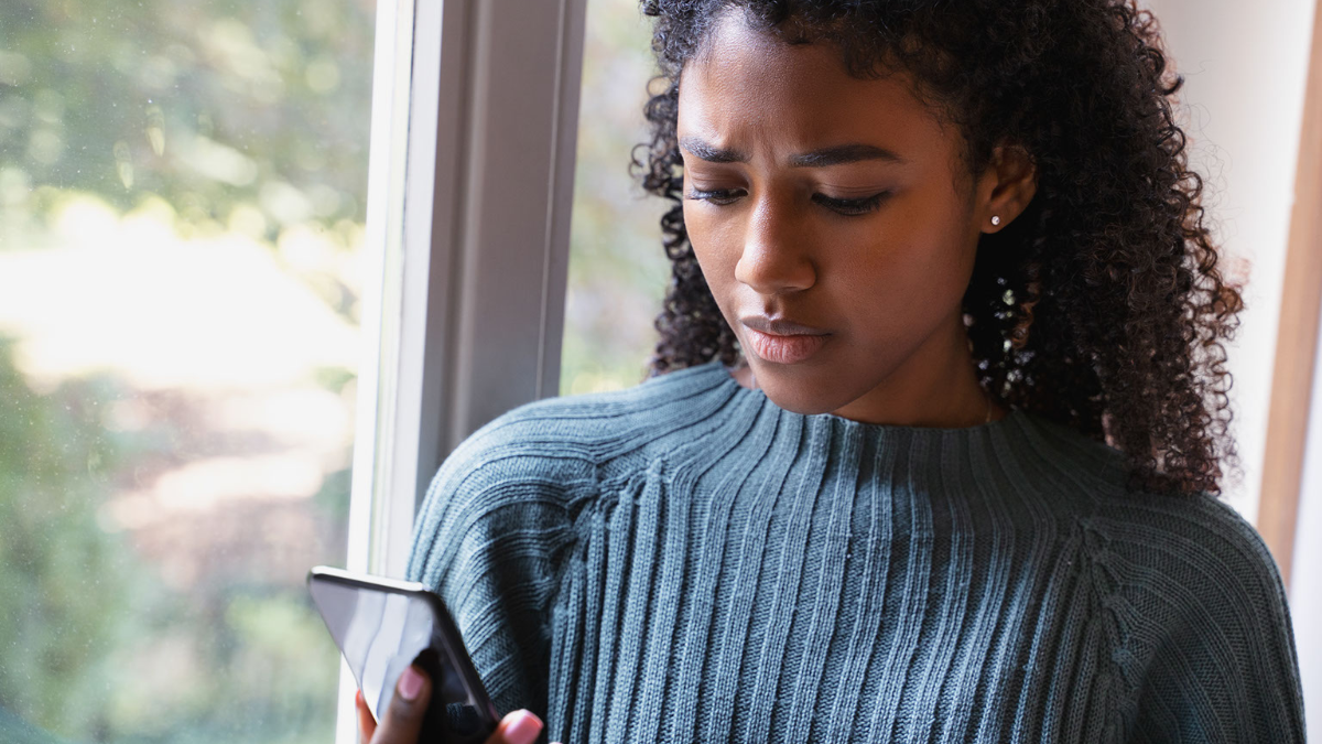 A Black woman wearing a blue sweater uses her cell phone to call her insurance agent to file a claim for damage to her bridal rings. 