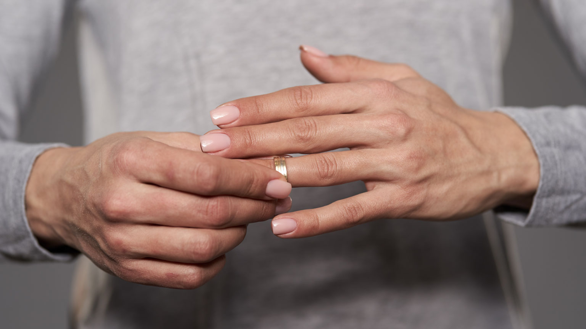 A woman removes her bridal rings from her left hand. 
