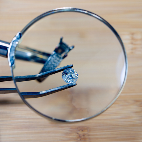 A custom design jeweler holds a diamond in grippers as part of a custom design bridal rings set. 