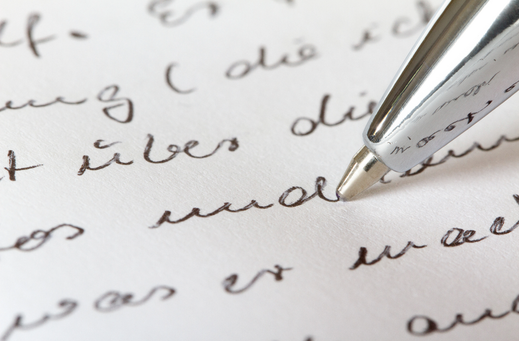 A pen traces cursive handwriting on a piece of paper.