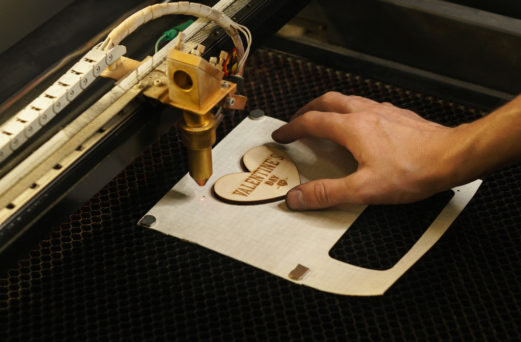 A laser engraving machine creates a design ona heart-shaped material.