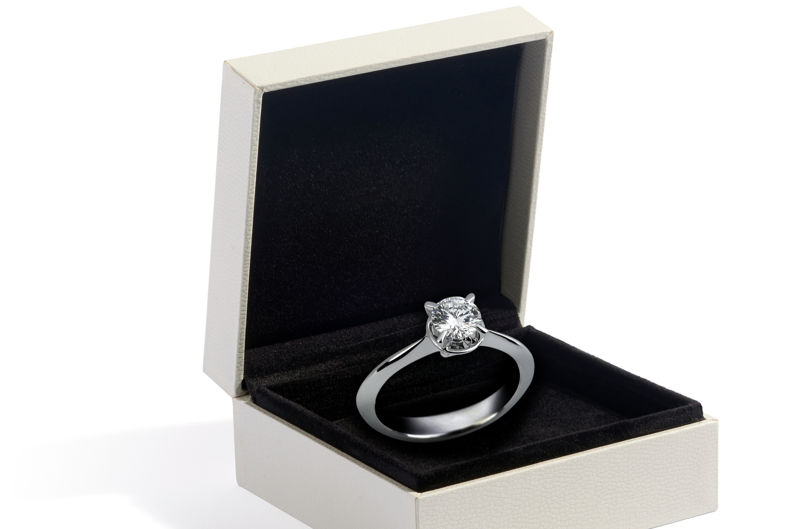 A white ring box with black velvet inside holds a diamond solitare engagement ring.