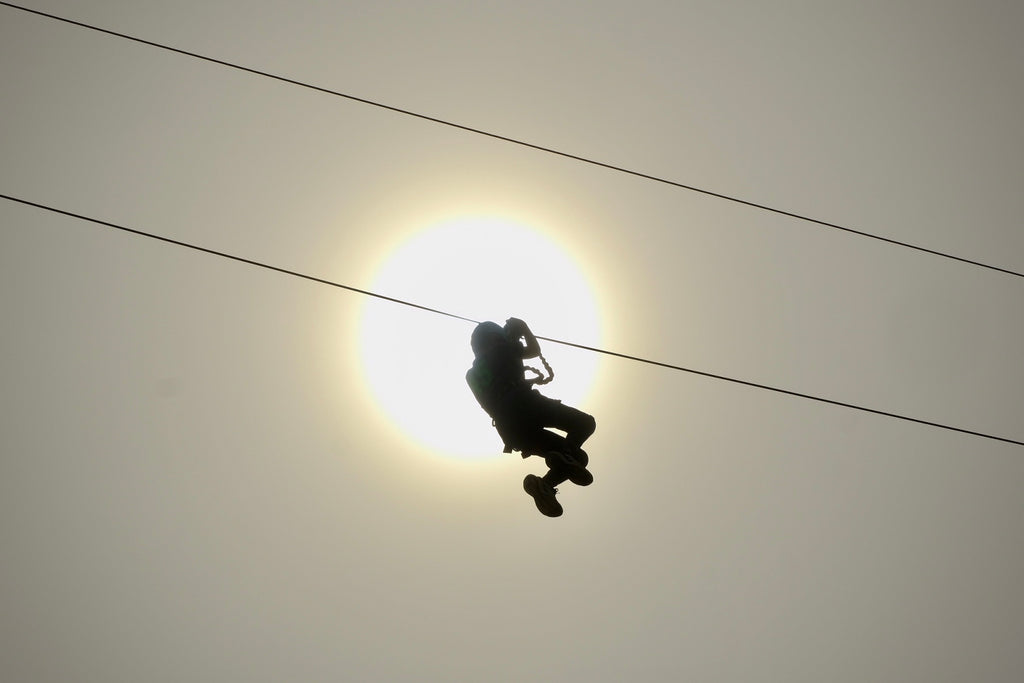 silhouette of person on zip wire speeding past the midday sun