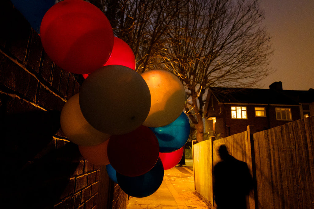 lone figure passes party balloons spilling over garden fence in a dark alleyway at dusk in Penge southeast London