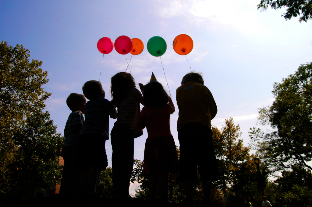 silhouettes of children gathered on a rock all holding colourful balloons in Inwood north Manhattan New York City