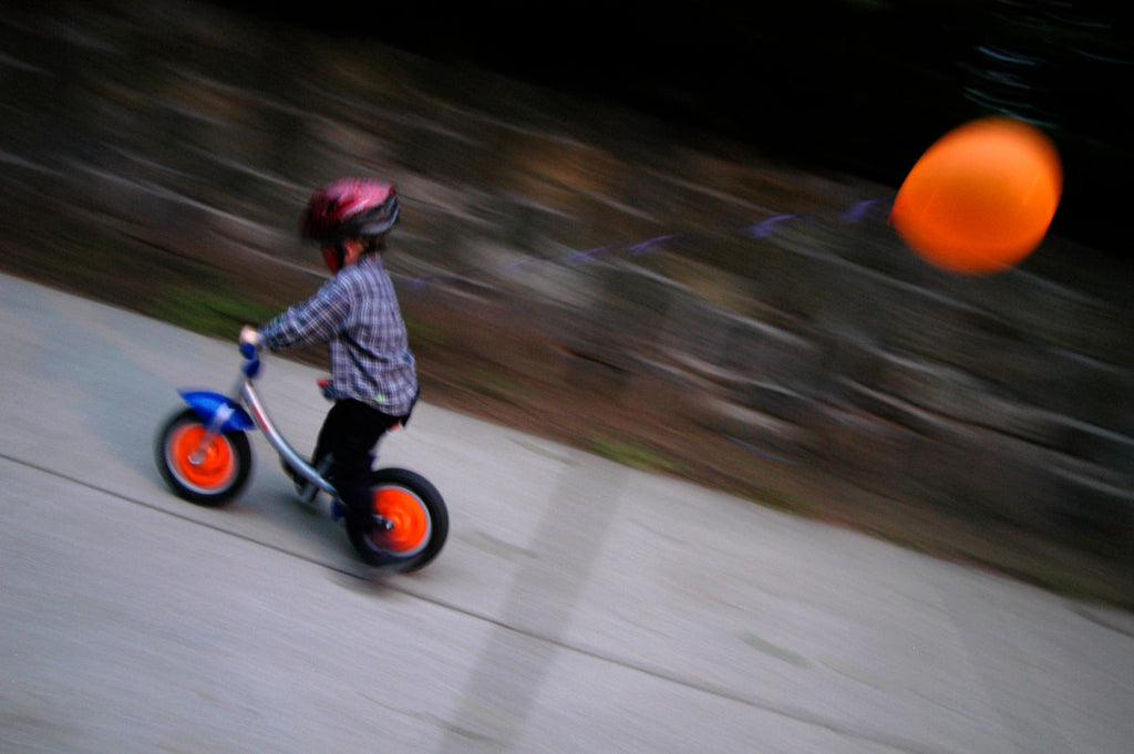 little boy speeding by on balance bike with orange balloon attached on a street in the Inwood neighbourhood in northern Manhattan New York City