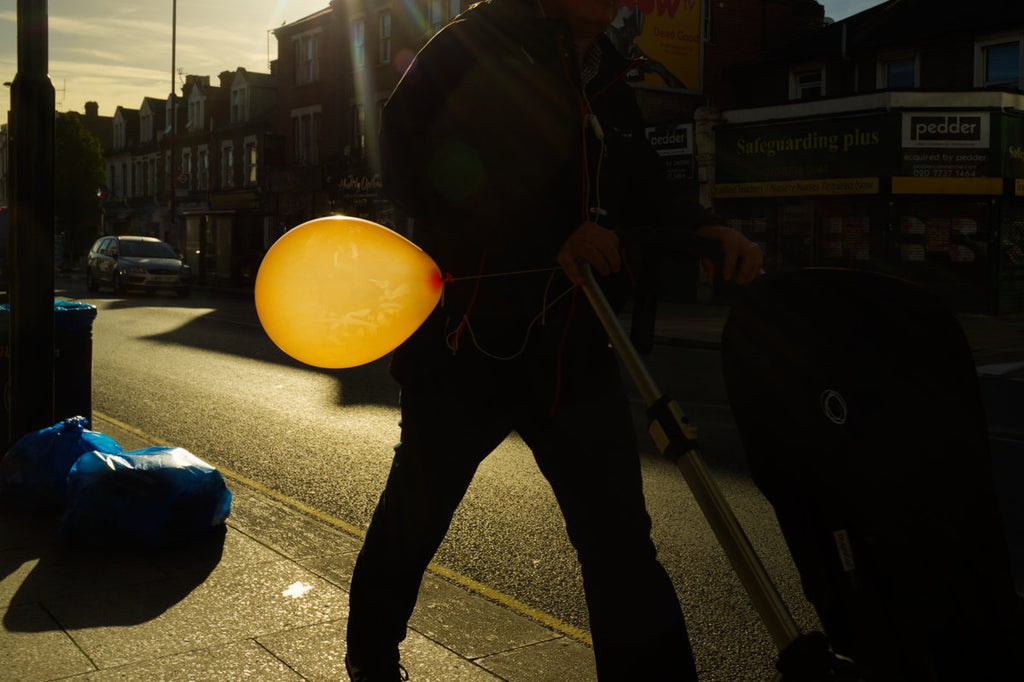 man pushing child's buggy with bright orange balloon attached on sunny day in Sydenham southeast London