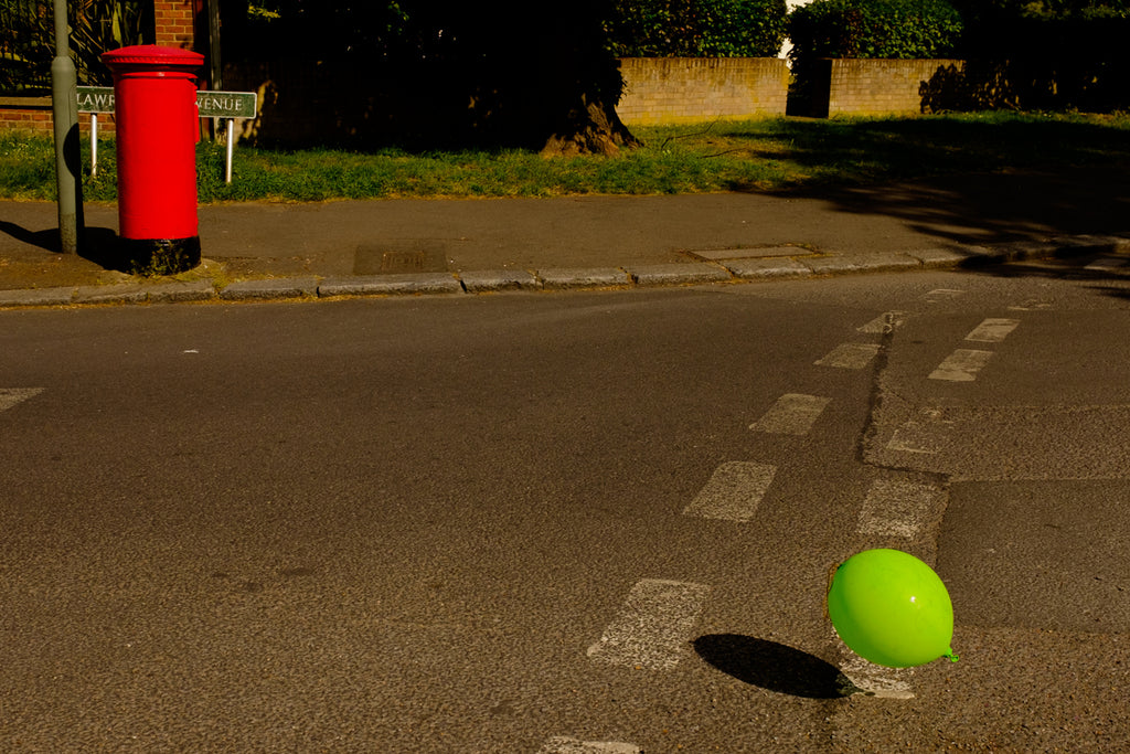 bright red post letter box and luminous green balloon on a street in southeast London