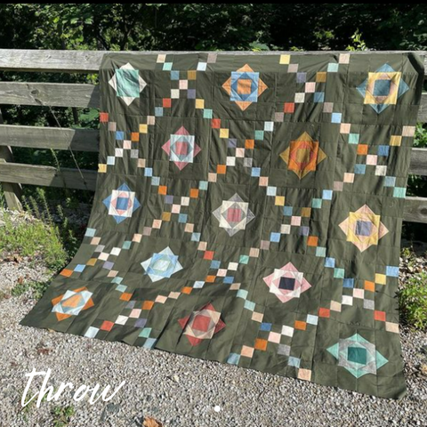 scrappy quilt on a grey background, displayed on a split rail fence