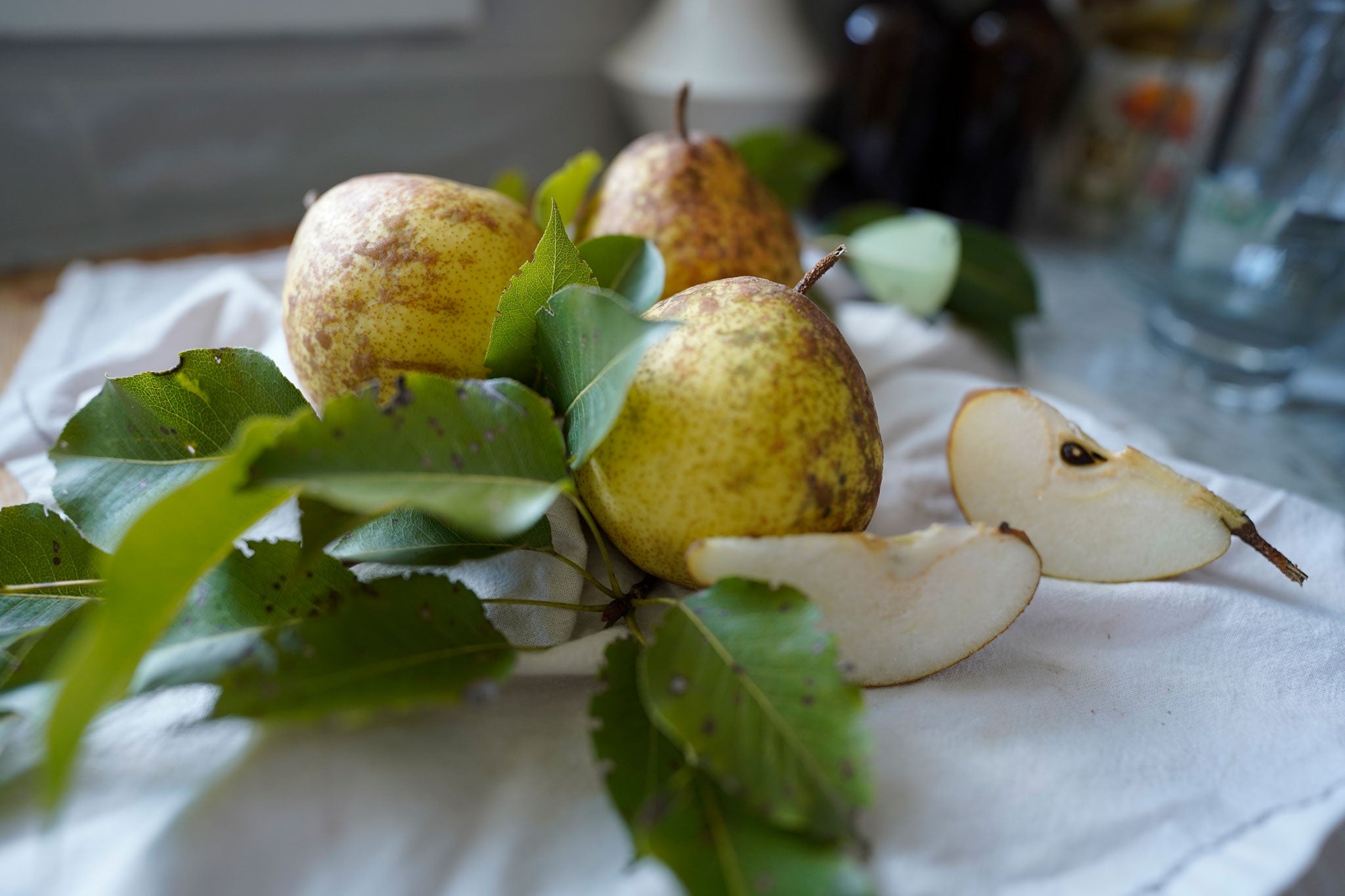Pears, pear leaves, and pear slices on white dish towel and wood cutting board on kitchen counter