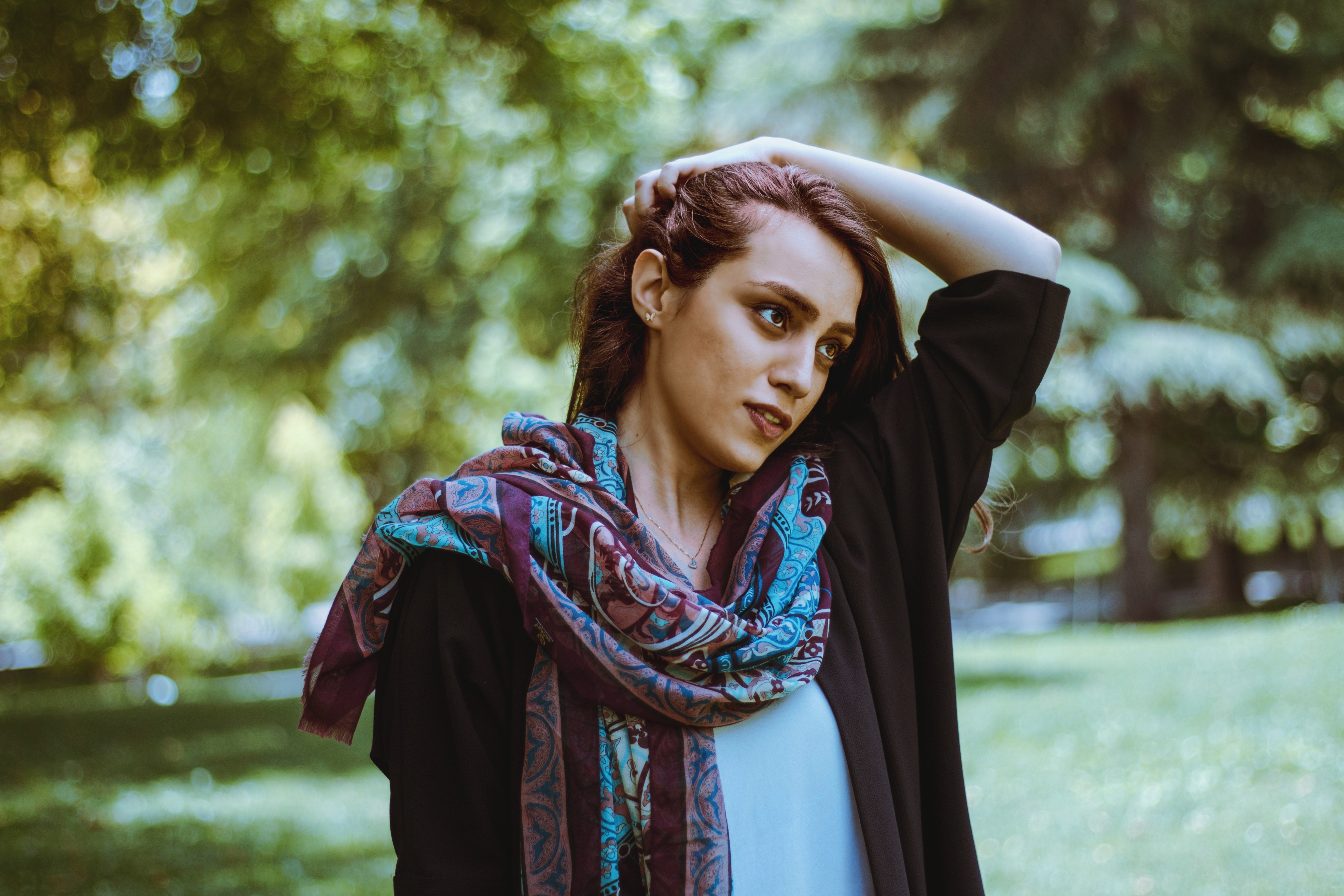 Woman wearing an asymmetrical drape scarf with a purple design in a park.