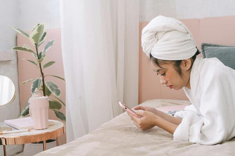 A woman in a bathrobe is using a mobile phone on the bed