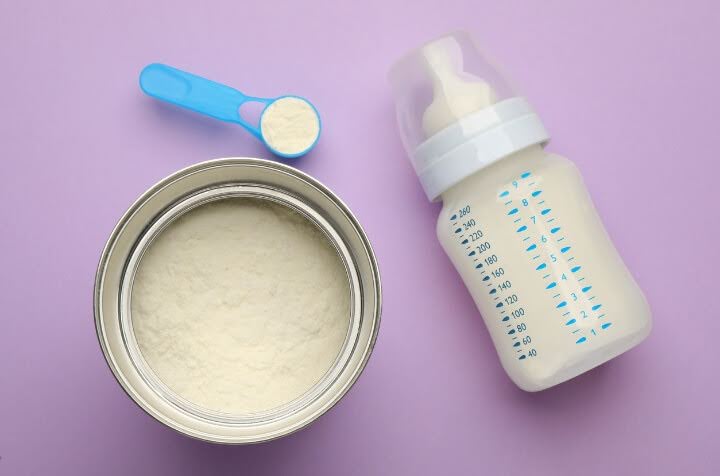 European goat milk formula in a bottle, with canister, and scooper.