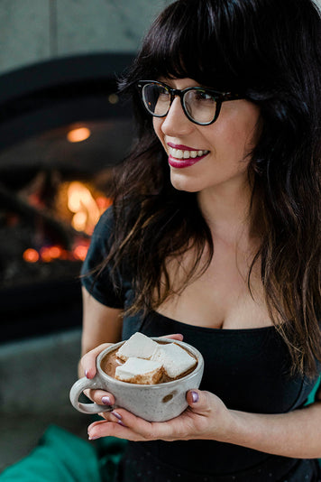 marshmallow girl smiling by fireplace with cup of hot cocoa