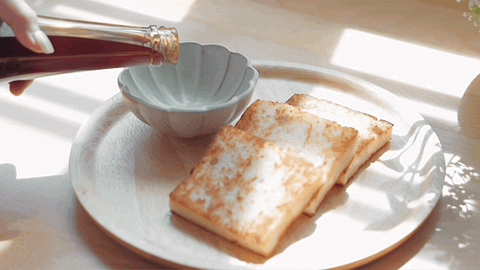 This picture is a dynamic picture. Sunlight on a wooden table, three fried radish cakes until golden brown on a round wooden plate, a hand is pouring white soy sauce paste