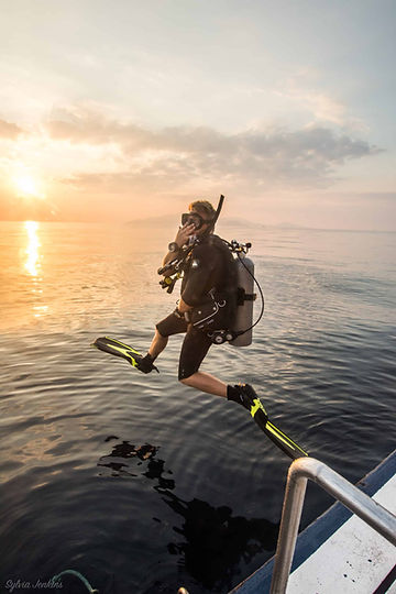 subacqueo che salta in acqua al tramonto per un'immersione notturna