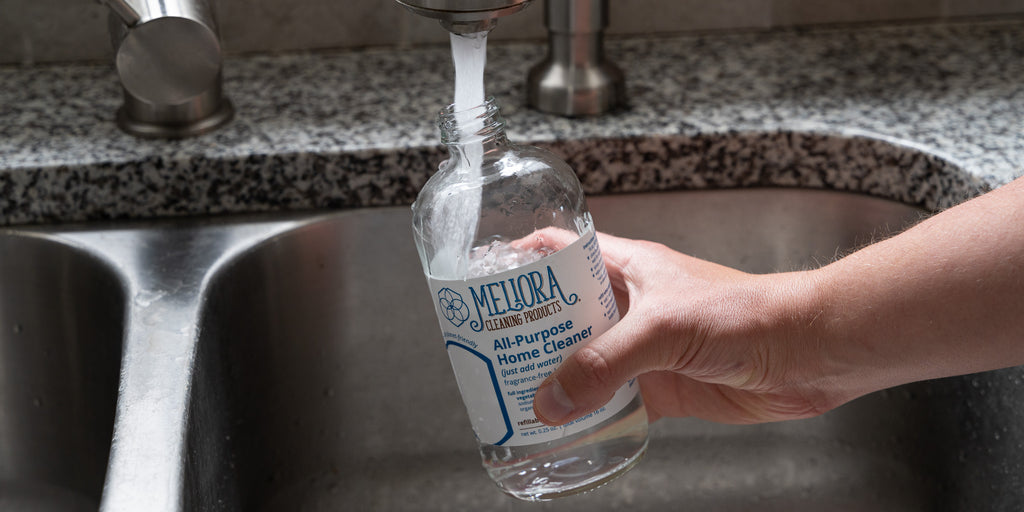 A person filling a Meliora all-purpose cleaner bottle with water from a faucet