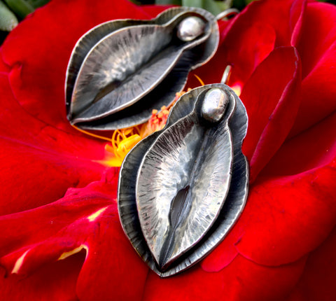 Zoe Zoe Jewelry's Sculptural Yoni Earrings, made with foldfoming and forging in sterling silver. They are large dangle earrings and are being displayed on a bright red flower