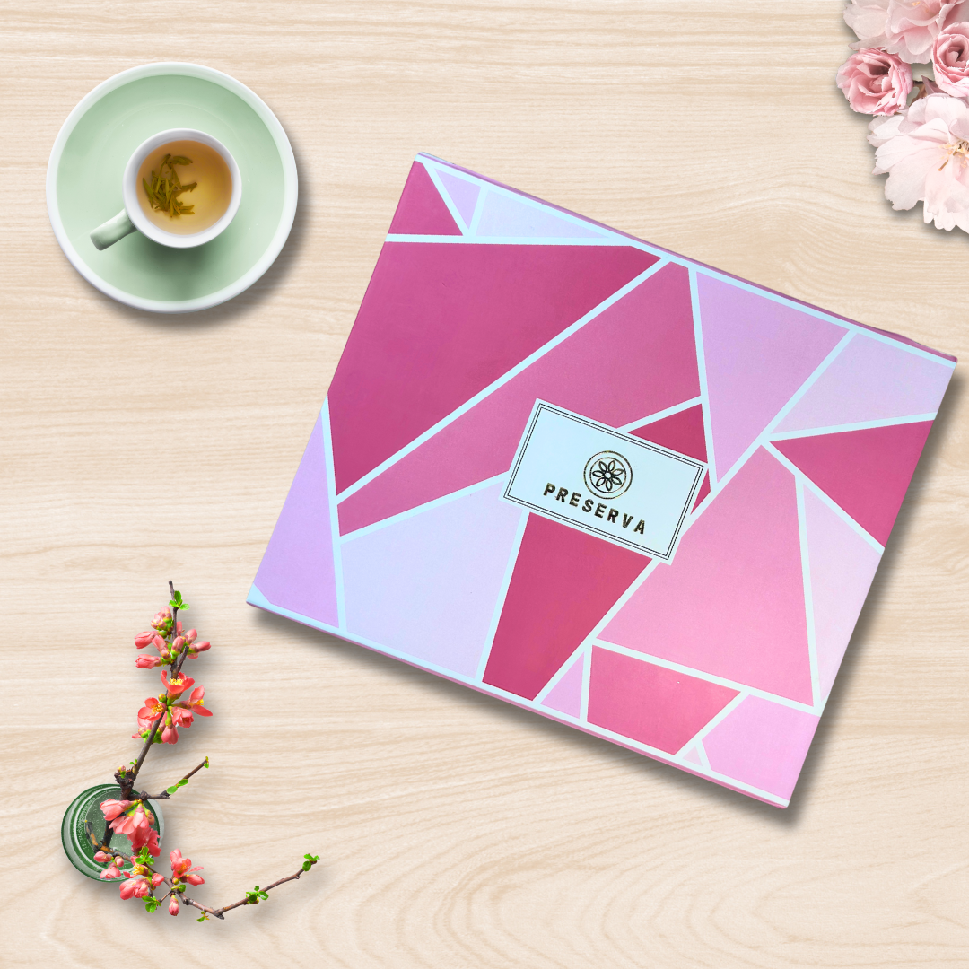 Pink Preserva Wellness Tea Gift Box with pattern on a wooden table next to tea in a cup and pink flowers