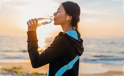 A woman drinking water from a plastic bottle on a beach