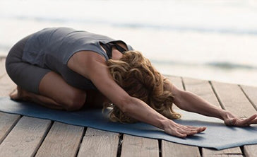 A person doing a yoga child pose outside on a mat
