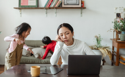 A woman being tired while working on a laptop or sleeping while her children playing in the back