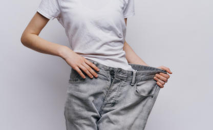 A slim person holding a loose jean which they are wearing