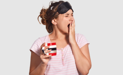 A woman yawning with her eyes closed and a cup in her hand