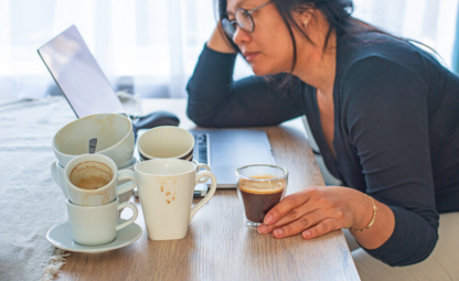 A lady tired and drinking coffees while working on a laptop