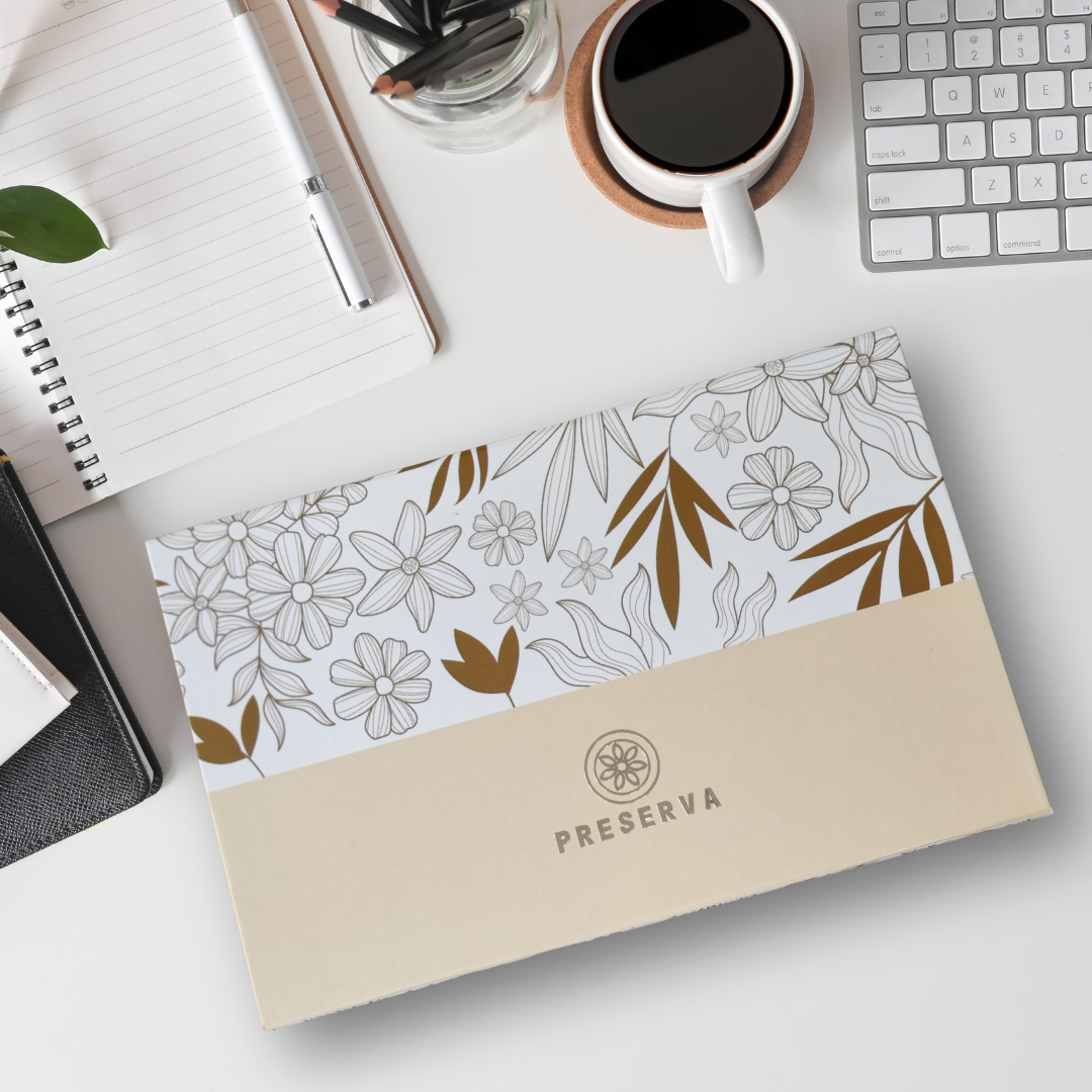 Preserva Wellness Tea Gift Box with floral pattern in gold colour in an office setup with keyboard, pen, notepad and coffee