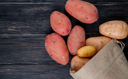 Red and brown sweet potatoes tossed from a jute bag
