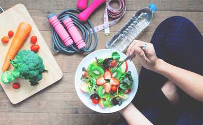 A plate full of healthy fruits and vegetables next to skipping rope, gym equipment, chopping tray, and water bottle