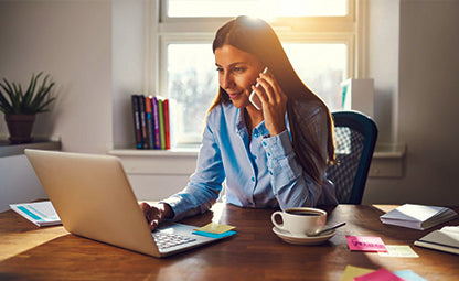 A lady working on the laptop while taking a call in the office