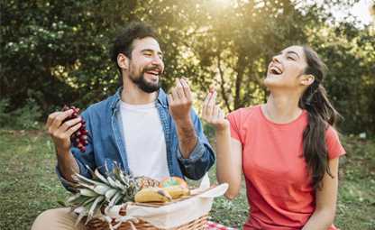 Two people sitting in a park and eating fruits from a picnic basket