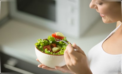 A woman eating a bowl of fresh and healthy fruits and vegetables