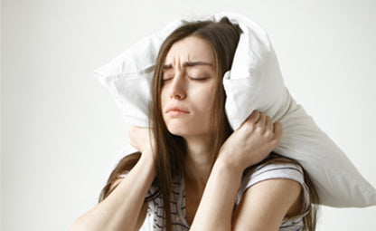 A stressed woman with difficulty sleeping, holding a pillow to her ears and eyes closed