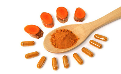 Sliced curcumin with powder in a wooden spoon next to vegan-friendly curcumin capsules