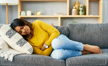 A woman holding her stomach in pain with closed eyes while lying down on a couch