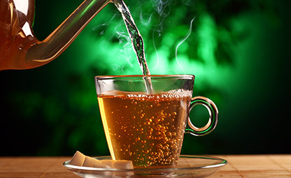 Pouring ginger tea from a glass pot into a cup