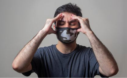 A man wearing a mask and pressing his head due to a headache