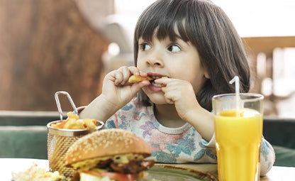 A kid eating unhealthy junk food like burgers, fries and sugary juice