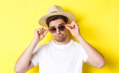 A man posing while wearing sunglasses and a hat on a yellow background