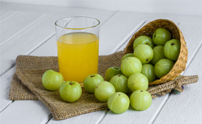 Organic Amla fruits tossed from a basket next to Amla juice