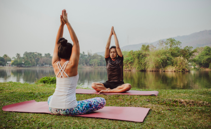 A couple doing Suryanamaskar yoga pose near the lake