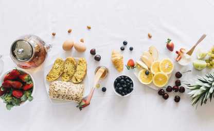  White table full of healthy foods like herbal tea, breads, berries, honey and fruits