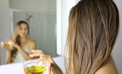 A person using hair oil from a glass bowl